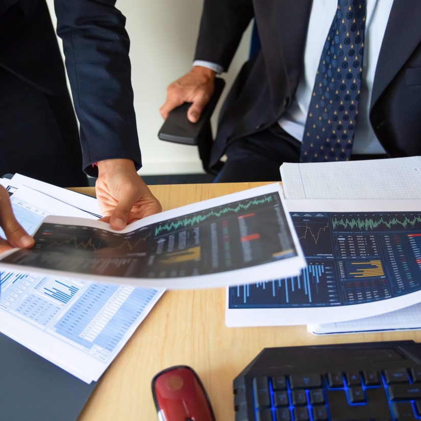 Investor and trader discussing statistic data, holding papers with financial charts and pen. Cropped shot. Broker job or trading concept