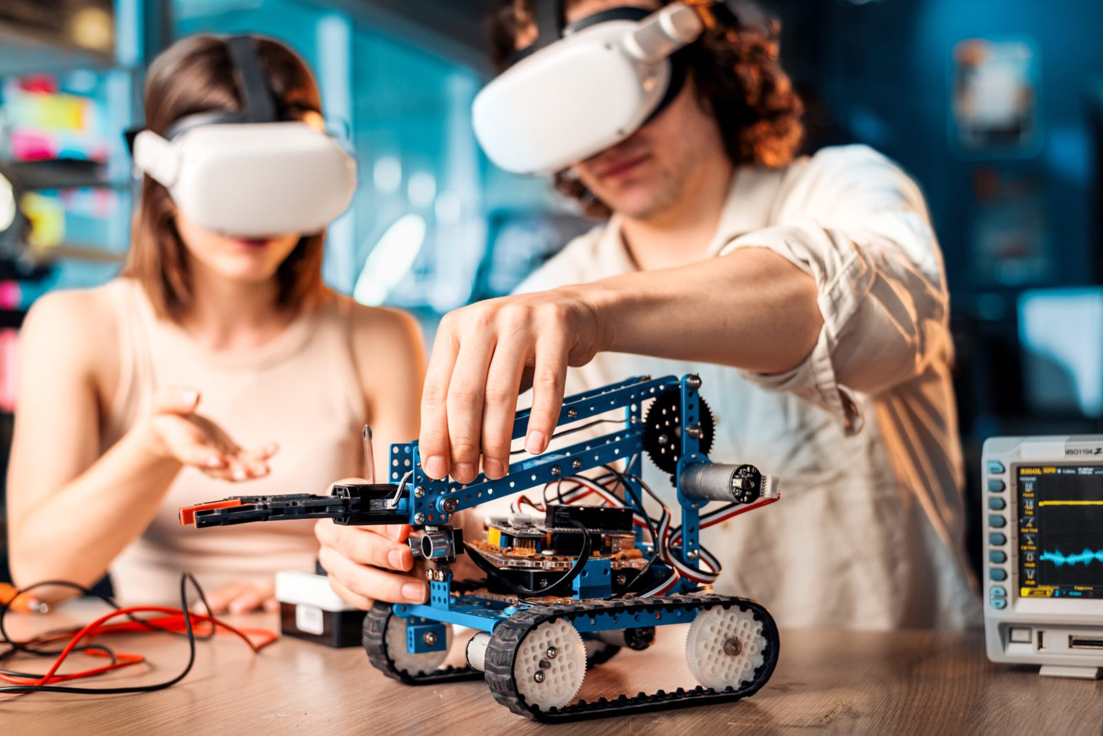 Young man and woman in VR glasses doing experiments in robotics in a laboratory. Robot and tools on the table
